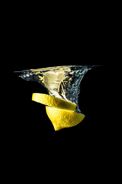 Lemon slices falling into the water close-up, macro, splash, bubbles, isolated on black  - Fotó, kép