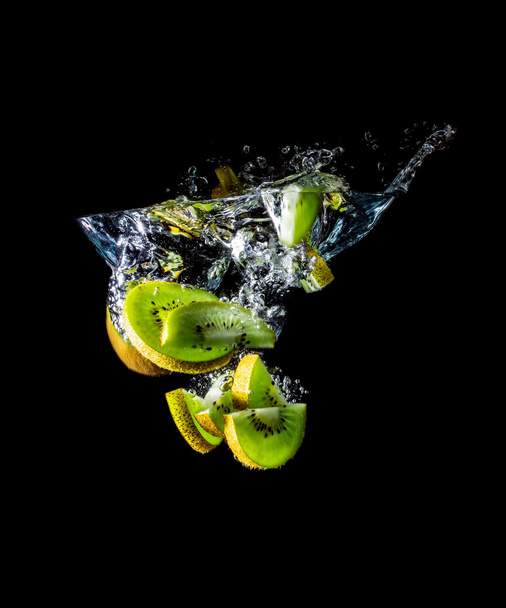 Kiwi slices falling into the water close-up, macro, splash, bubbles, isolated on black  - Foto, afbeelding