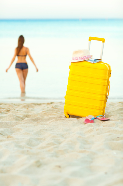 Желтый чемодан на пляже и девушка входит в море в й
 - Фото, изображение