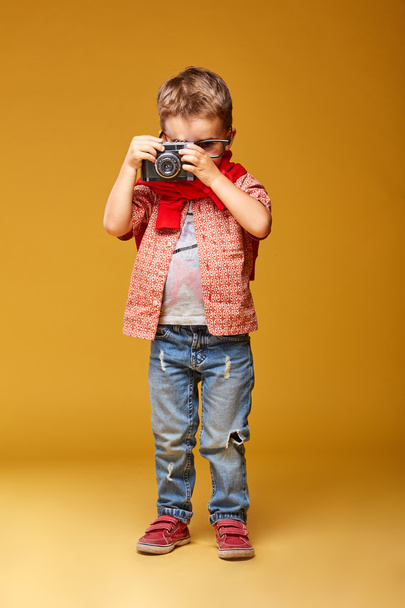 Χαριτωμένο μικρό αγόρι με τη φωτογραφική μηχανή στο studio με κίτρινο φόντο - Φωτογραφία, εικόνα