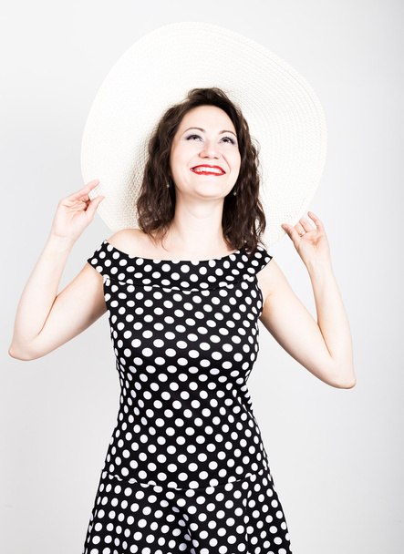 beautiful young brunette woman holding a broad-brimmed hat, she expression of different emotions. wears a dress with polka dots - Фото, изображение