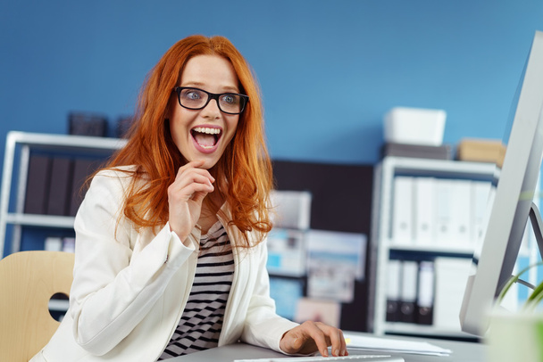 Thrilled young woman working at desk on computer - Foto, Bild