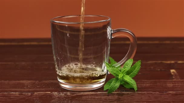Tea being poured into glass tea cup and mint leaves on brown wooden table - Footage, Video