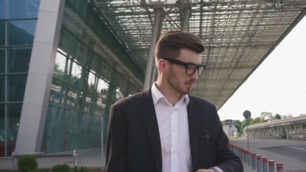 Close-up of handsome nervous businessman in glasses waiting for his retarded flight. Modern airport background - Metraje, vídeo