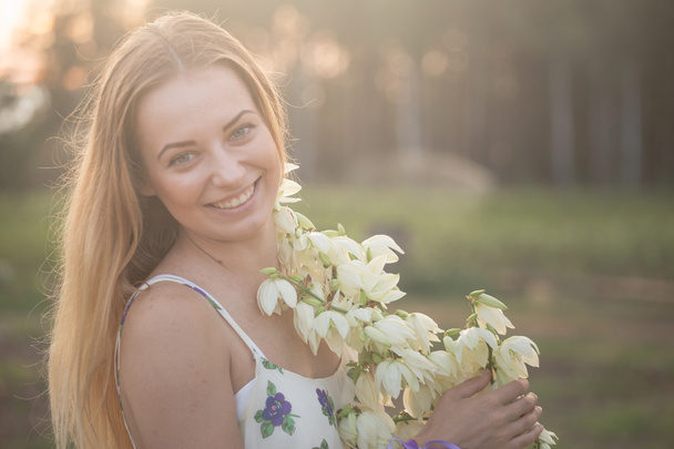 Close-up πορτρέτο... Όμορφη όμορφη κοπέλα που θέτουν σε μακρύ φόρεμα ενάντια στο πεδίο με τα άσπρα λουλούδια - Φωτογραφία, εικόνα