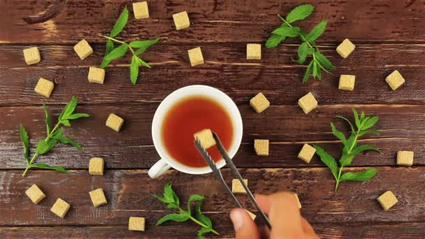 Cubos de açúcar adicionados em vidro de chá na mesa com folhas de hortelã fresca e açúcar mascavo em cubos na mesa de madeira marrom
 - Filmagem, Vídeo