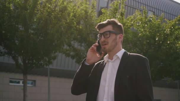 Young attractive businessman talking on mobile phone on the street background - Video