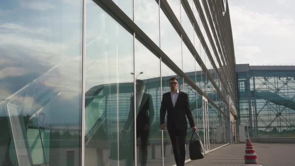 Attractive young bearded businessman in glasses goes for boarding to his plane. Glass airport wall background - Záběry, video
