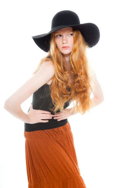 Handsome girl with long red hair wearing black shirt and brown dress and black hat. Fashion studio shot isolated on white background. - Foto, Bild