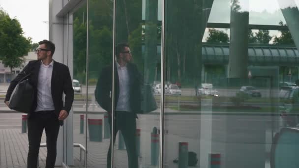 Young confident businessman with suitcase in modern airport terminal on the glass wall background. Travelling hipster guy concept - Filmagem, Vídeo