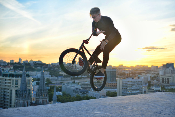 Mann springt auf Fahrrad und vollführt einen Trick gegen den Sonnenuntergangshimmel. Extremsport - Foto, Bild