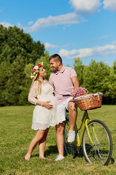 Loving pregnant couple in park embracing summer, kisses, smiles  - Foto, afbeelding
