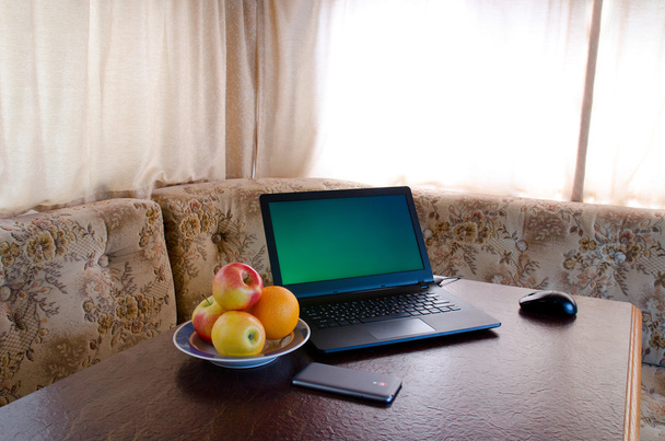 Side view of a laptop in a cozy kitchen with a plate of fruit, a smartphone. Break - Photo, Image