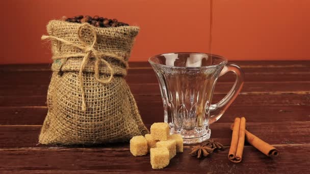 テーブルの上のコーヒー カップを注ぐ上に位置するコーヒー豆バーラップ袋、ブラウン シュガー キューブ、シナモンスティックで茶色の木製のテーブル - 映像、動画