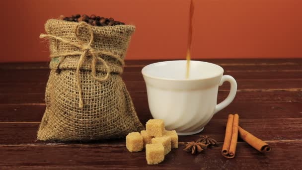 Despeje uma xícara de café na mesa localizada grãos de café em saco de serapilheira, cubos de açúcar mascavo e paus de canela sobre mesa de madeira marrom
 - Filmagem, Vídeo