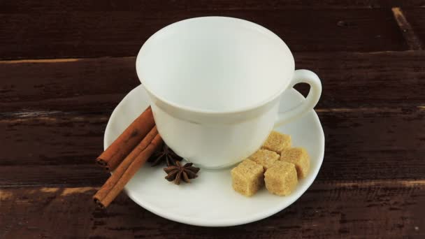 Наливаємо чашку кави кавовими зернами на тарілку, коричневі цукрові кубики та палички кориці на коричневий дерев'яний стіл
 - Кадри, відео