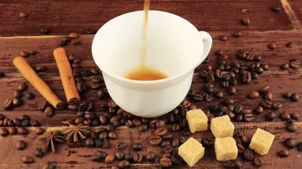 Öntés egy csésze kávét a táblázat fölötti szemes kávé, kockák barna cukor, és fahéjat barna fából készült asztal - Felvétel, videó