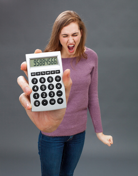 enraged young woman screaming against financial economy on oversized calculator - Foto, imagen