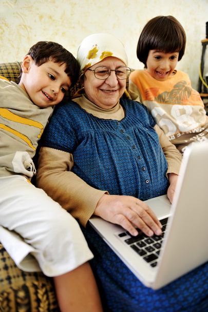 Пожилая женщина работает на ноутбуке в доме с внуком
 - Фото, изображение