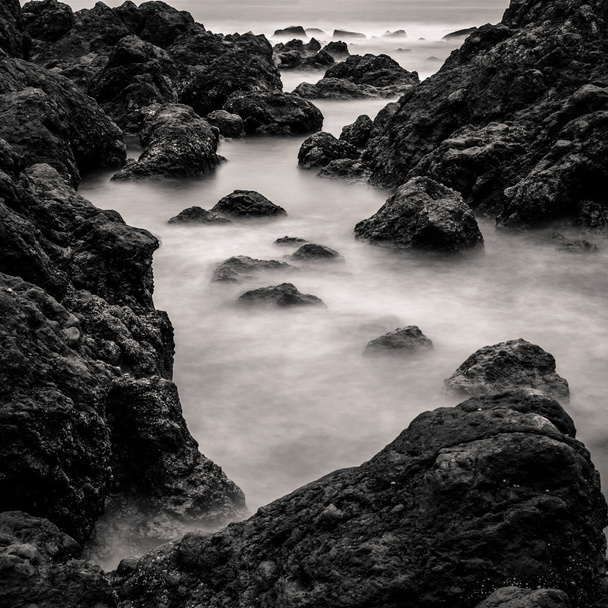 bewegingsonscherpte water omringende rotsen, zwart-wit - Foto, afbeelding