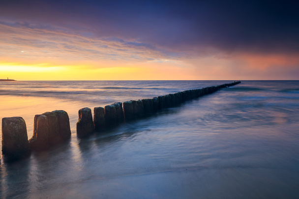 ηλιοβασίλεμα στην παραλία με ένα ξύλινο κυματοθραύστη, μακροχρόνια έκθεση - Φωτογραφία, εικόνα