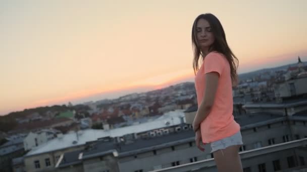 Gyönyörű mosolygó nő táncol, hosszú fúj a haj és a fegyvergyűjtés a naplementében az apartmanok tető - Felvétel, videó
