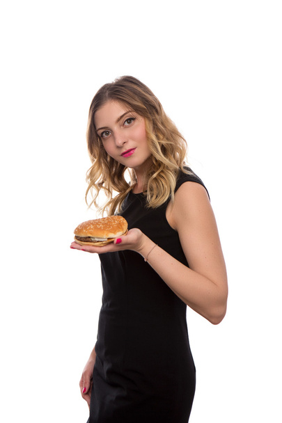 young beautiful girl in a black dress with a Burger in hand isolated on white background - Foto, Imagen