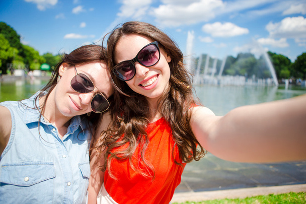 Kaukasische meisjes maken selfie achtergrond grote fontein. Jonge toeristische vrienden reizen op vakantie buitenshuis glimlachend gelukkig. - Foto, afbeelding