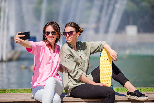 Καυκάσιες κοπέλες κάνουν selfie φόντο μεγάλο σιντριβάνι. Νέοι τουριστικοί φίλοι ταξιδεύουν σε διακοπές σε εξωτερικούς χώρους χαμογελαστός. - Φωτογραφία, εικόνα