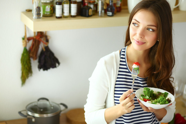 Young woman eating salad and holding a mixed salad - Valokuva, kuva