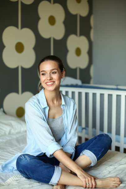 Young woman sitting on the bed near childrens cot. - Foto, immagini