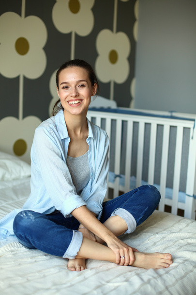 Young woman sitting on the bed near childrens cot. - Fotoğraf, Görsel