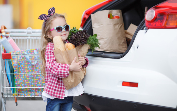 Meisje met een winkelwagentje vol boodschappen in de buurt van de auto - Foto, afbeelding