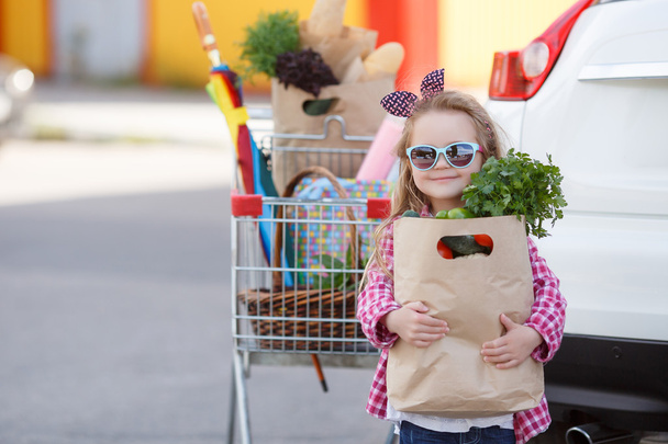 Girl with a shopping cart full of groceries near the car - Fotó, kép