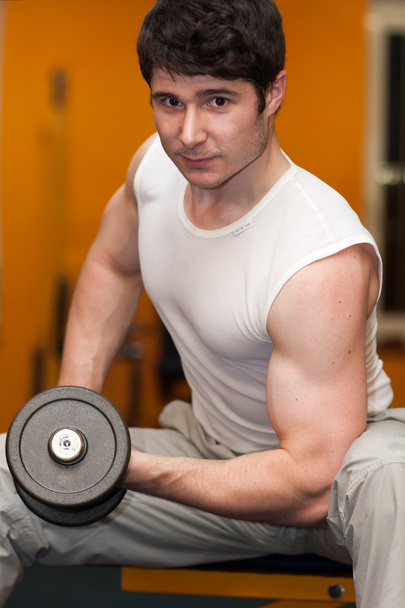 Young man lifting dumbell at fitness gym - Photo, Image