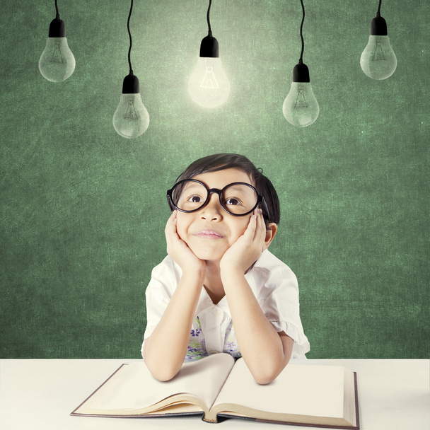 Kid thinking solution under lightbulb - Фото, изображение