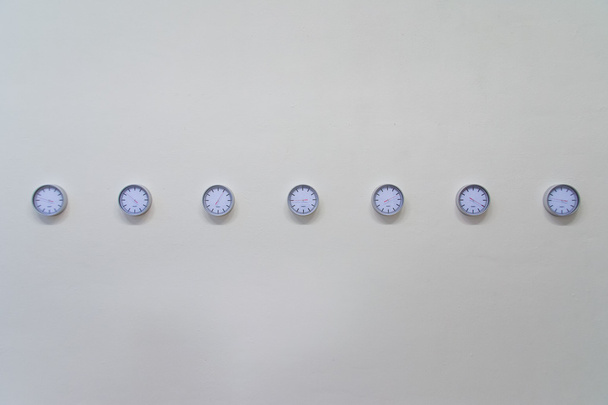Seven Clocks Hanging in Row on Plain White Wall - Foto, immagini