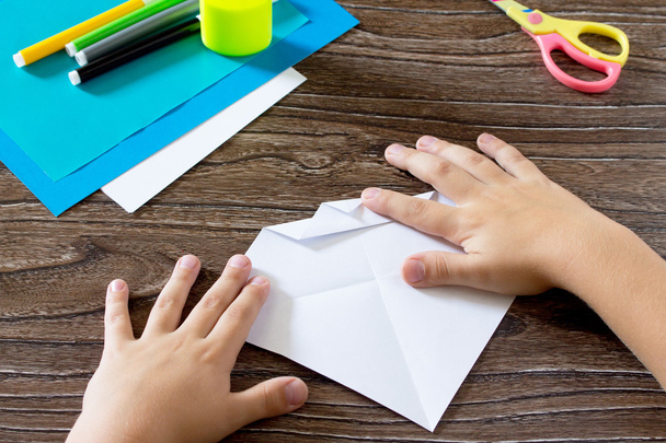Το παιδί κατέχει ένα τετράγωνο λωρίδα χαρτί και διπλώστε την γωνία. Το chi - Φωτογραφία, εικόνα