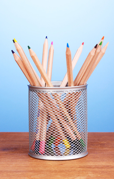 Color pencils in glass on wooden table on blue background - 写真・画像