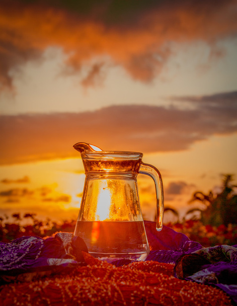 Um jarro de água potável em um fundo de um pôr-do-sol esplêndido
 - Foto, Imagem