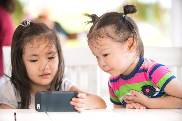 маленькая азиатская девочка ищет сотовый телефон со своей сестрой
 - Фото, изображение