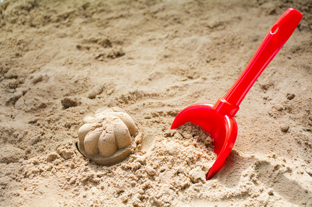 red toy bucket and molded sand in a sandbox or at the beach - Фото, зображення