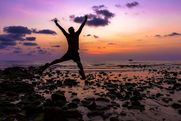 Happy man met zijn handen omhoog springen tijdens zonsondergang op het strand - Foto, afbeelding