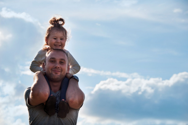 La hija feliz sobre sus hombros al padre contra el cielo
 - Foto, Imagen