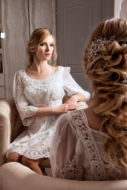 The blond haid bride sitting in white dress neat the mirror - Fotó, kép