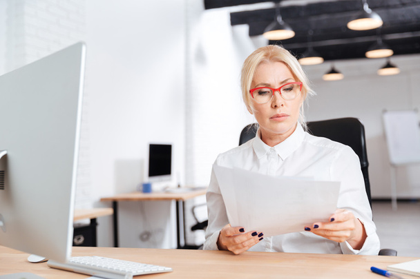 Beautiful mature businesswoman reading papers in office - Zdjęcie, obraz