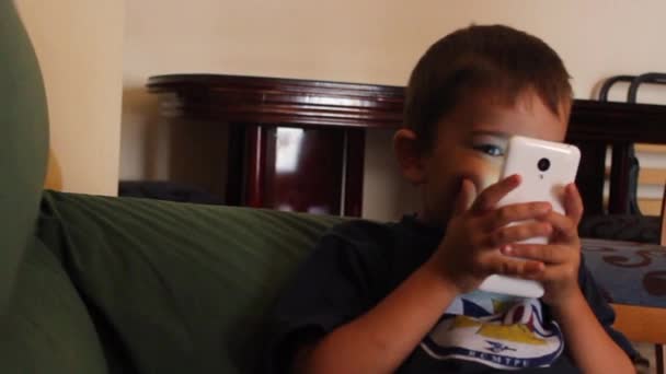 Kleiner Junge spielt mit Handy auf dem Bett liegend - Filmmaterial, Video