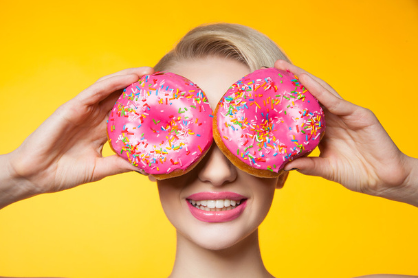 Short-haired model covering eyes behind two pink donuts - Fotografie, Obrázek