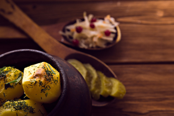 Baked potato in old pot on wooden background with pickled cabbage and cucumber - Photo, image