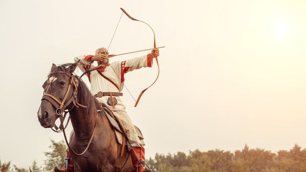 Man in ethnic clothing is riding a horse and aiming from the bow - Foto, afbeelding